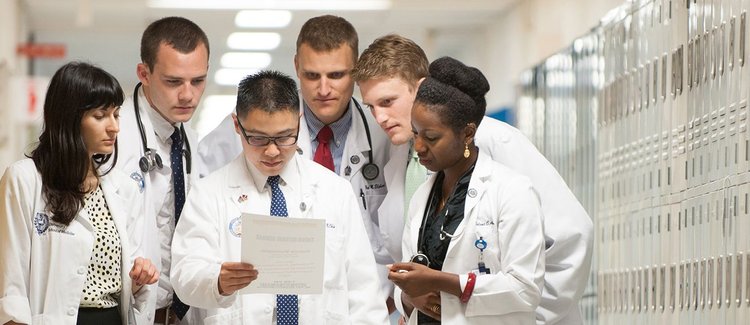 A group of diverse medical students leaning in to read a single document.