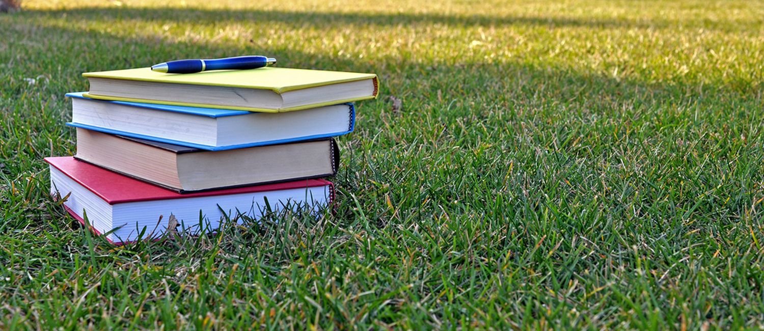 stack of books on a wide campus lawn