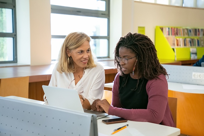 female student completing assignment in library with tutor