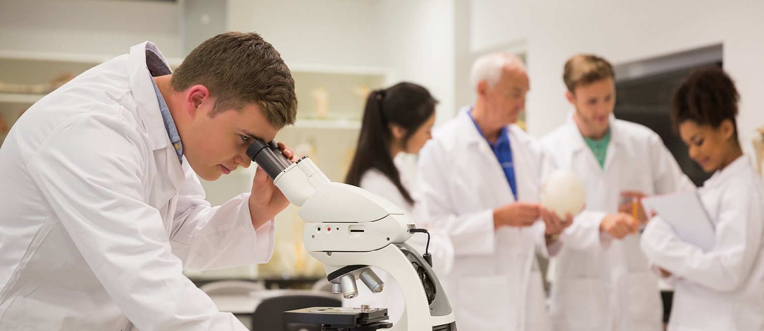 medical student working with microscope with colleagues in the background