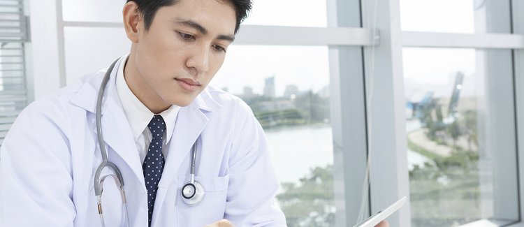 A young doctor in a white jacket looking at a tablet.