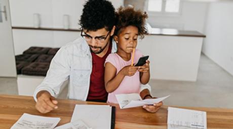 A parent looking at bills while holding a child using a calculator