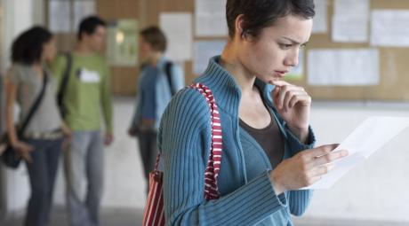 young woman standing in hallway, reading sheet of paper, side view