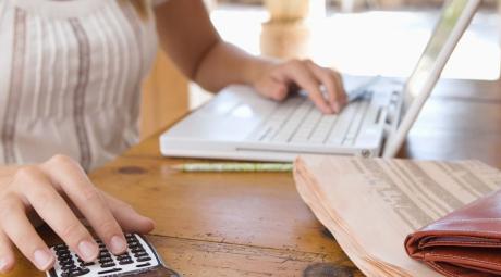 young woman at dining room table with laptop, calculator and wallet