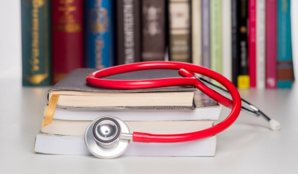 A red stethoscope on top of a stack of books