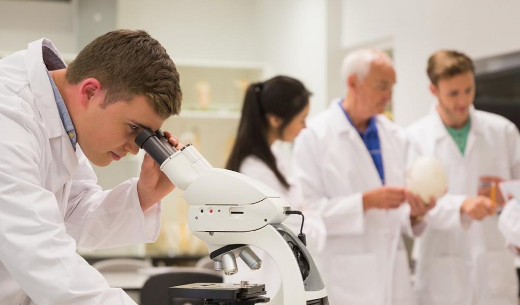 medical student working with microscope with colleagues in the background