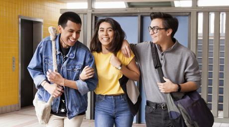 Three students carrying bags walk in a hallway