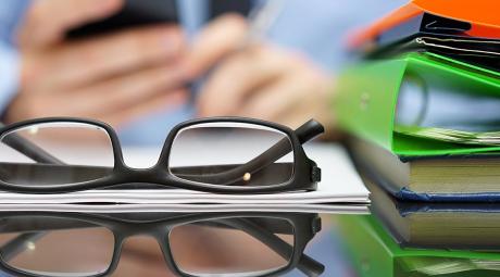 Person in background on phone with eyeglasses and books sitting on desk in foreground