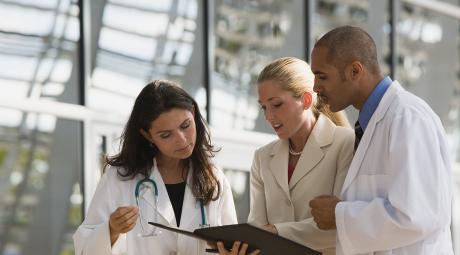two people in white coats, one in a suit looking at documents in a folder