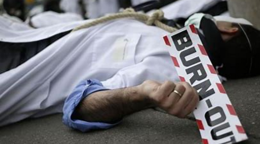 Stressed doctor lying with a sign that says burn out