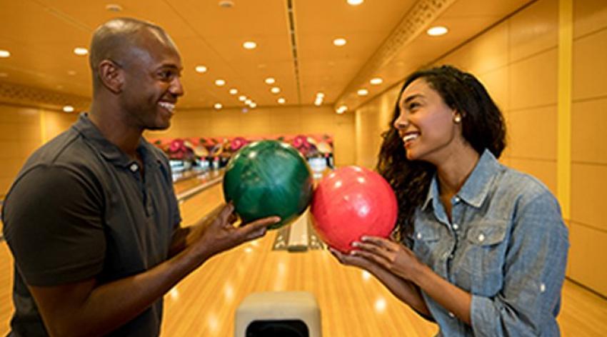 A couple looking at each other while holding bowling balls