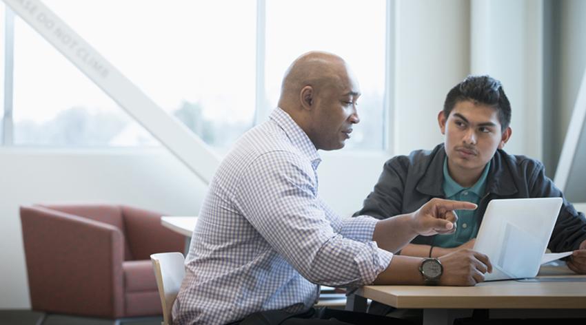 An advisor speaks to a student while sitting at a table