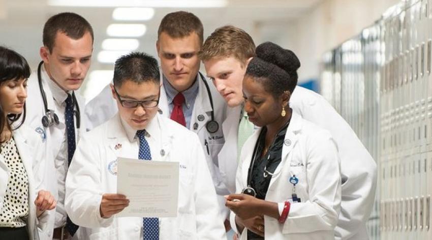 A group of diverse medical students leaning in to read a single document.