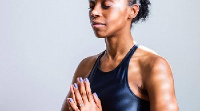 An individual wearing workout gear sits straight up with their eyes closed and hands in a prayer position. 