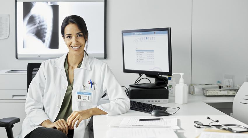 A doctor in a white coat sits at a desk