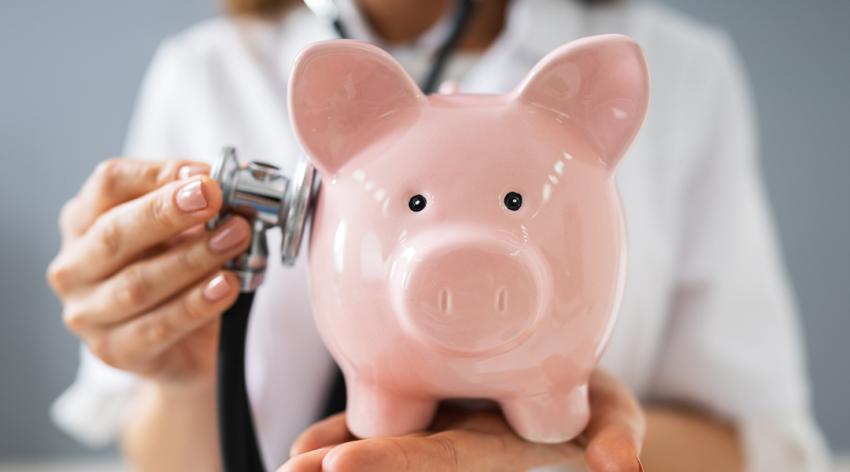 A doctor holds a stethoscope up to a piggy bank
