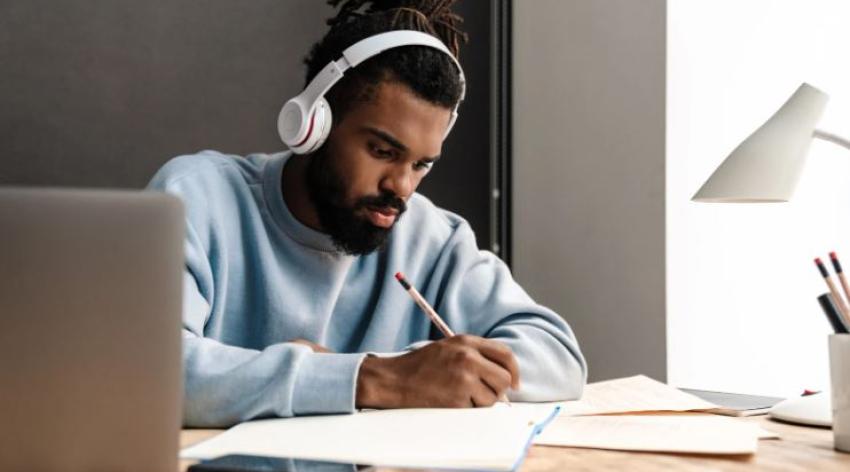 College student studying with headphones on and laptop in background